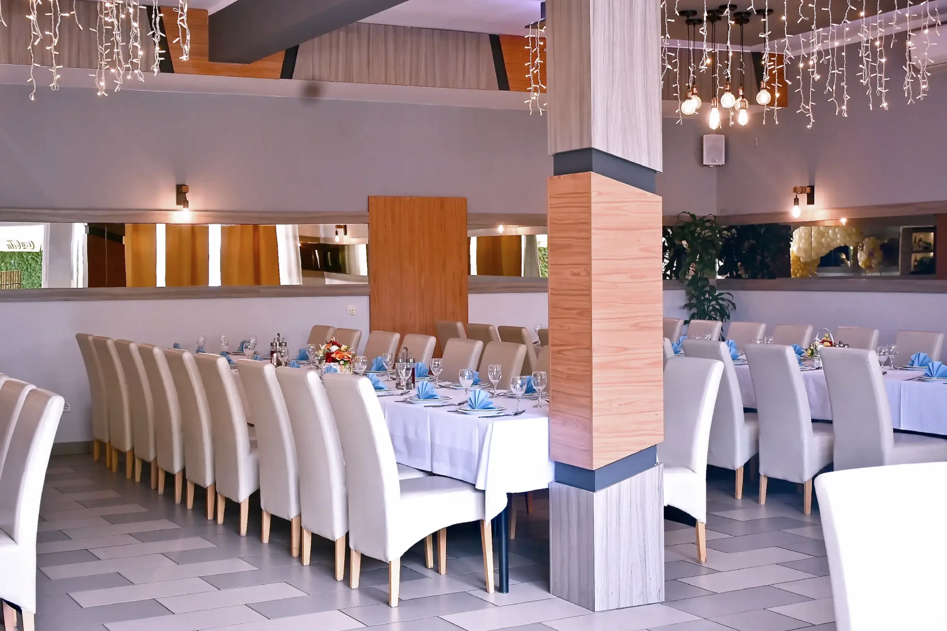 Kod Bosanca velika sala sa redovima posloženih stolaca i stolova priređenih za događanje (bijeli tanjuri, beštek i modre salvete) sa redovima posloženih stolaca i stolova priređenih za događanje (bijeli tanjuri, beštek i modre salvete)