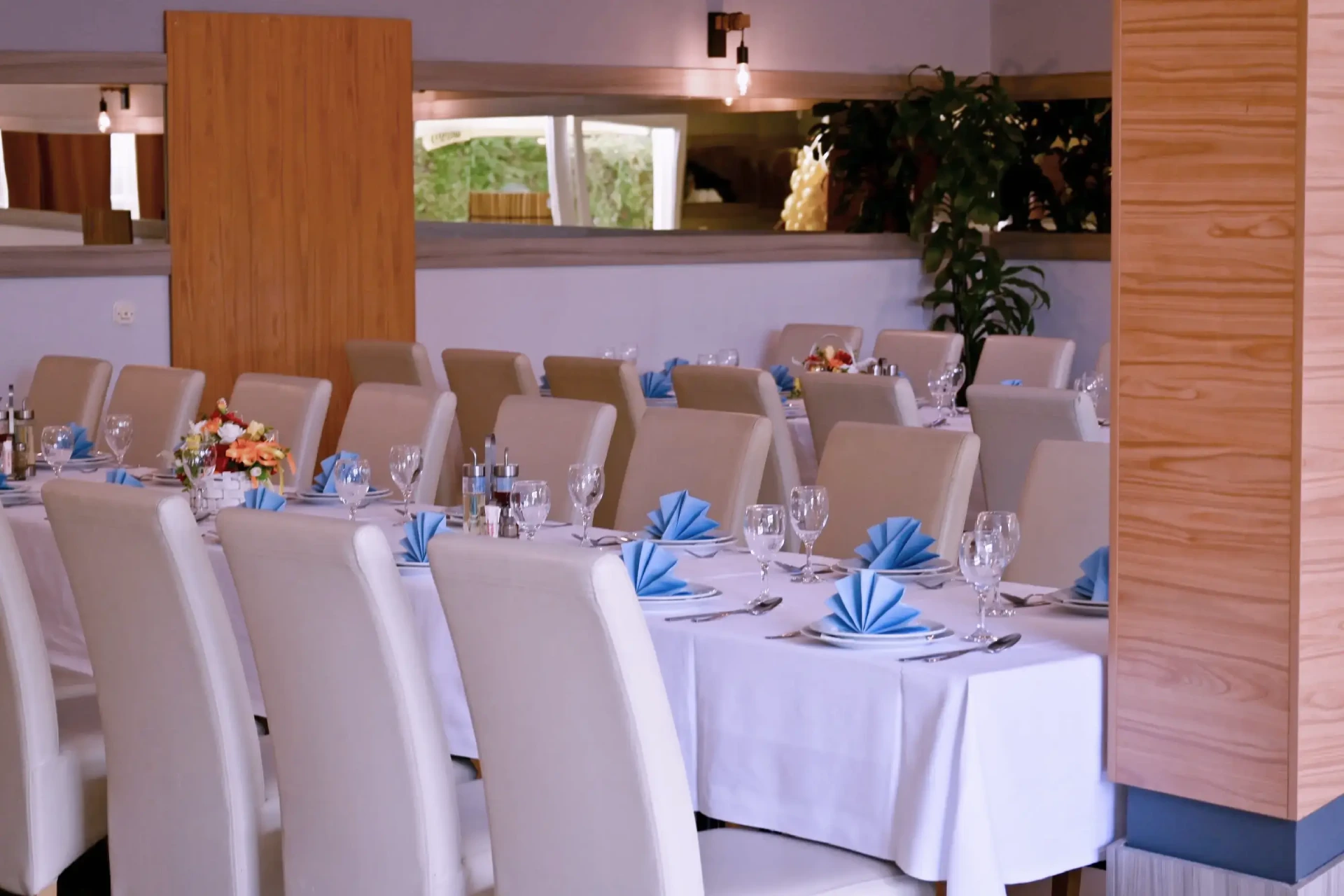 Kod Bosanca velika sala sa redovima posloženih stolaca i stolova priređenih za događanje (bijeli tanjuri, beštek i modre salvete) sa redovima posloženih stolaca i stolova priređenih za događanje (bijeli tanjuri, beštek i modre salvete)