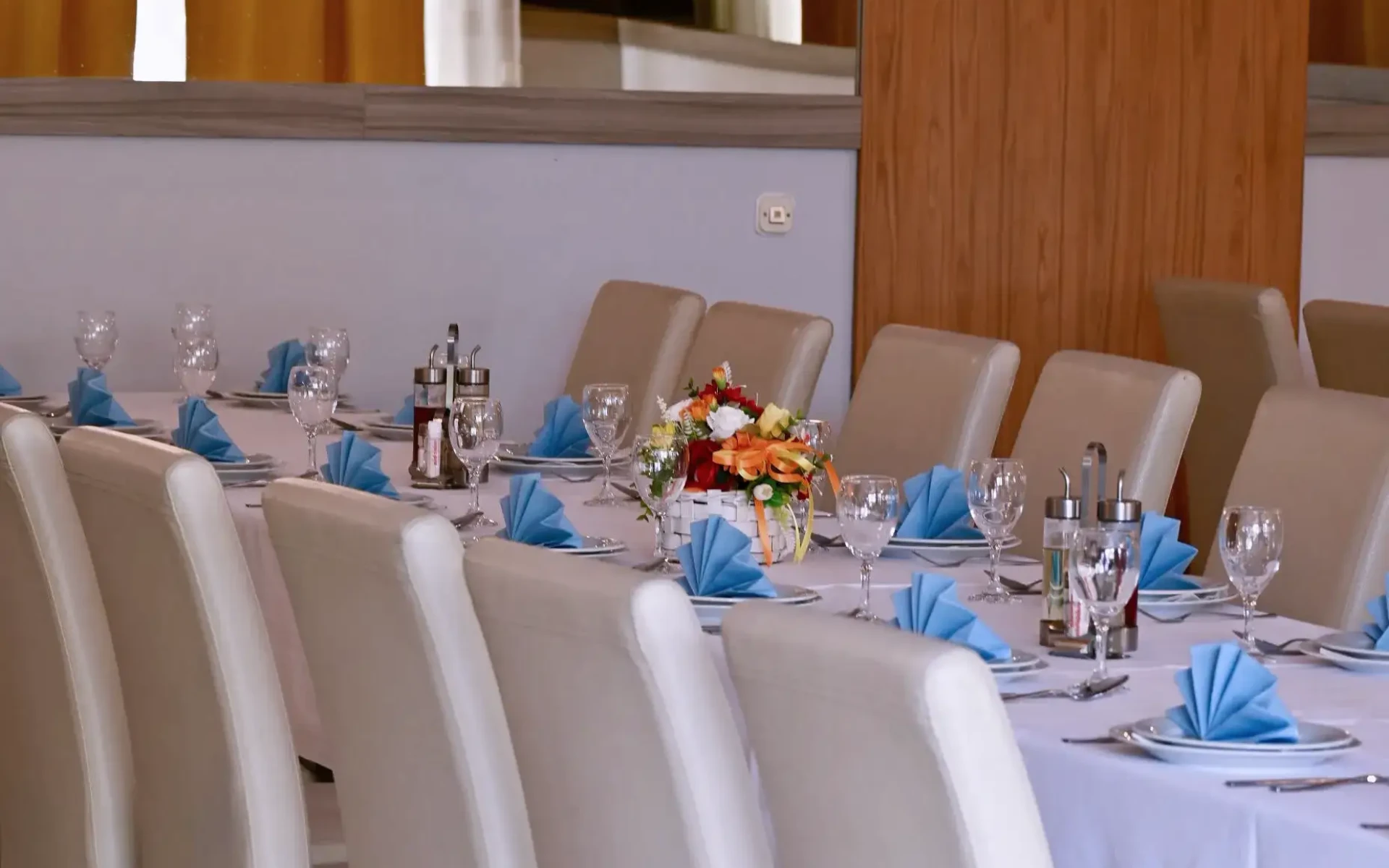 Kod Bosanca velika sala sa redovima posloženih stolaca i stolova priređenih za događanje (bijeli tanjuri, beštek i modre salvete) sa redovima posloženih stolaca i stolova priređenih za događanje (bijeli tanjuri, beštek i modre salvete)