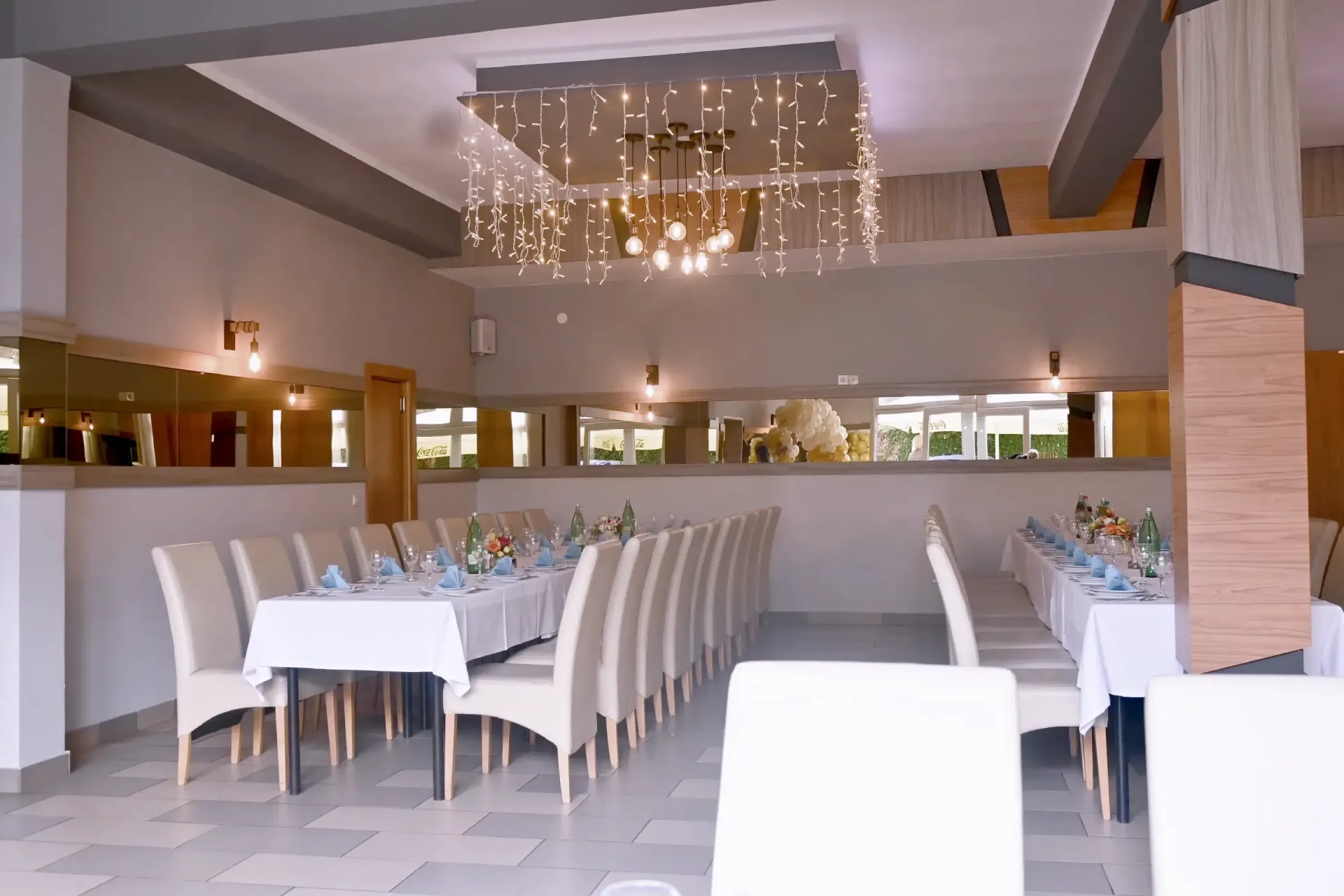 Kod Bosanca velika sala sa redovima posloženih stolaca i stolova priređenih za događanje (bijeli tanjuri, beštek i modre salvete) sa redovima posloženih stolaca i stolova priređenih za događanje (bijeli tanjuri, beštek i modre salvete)