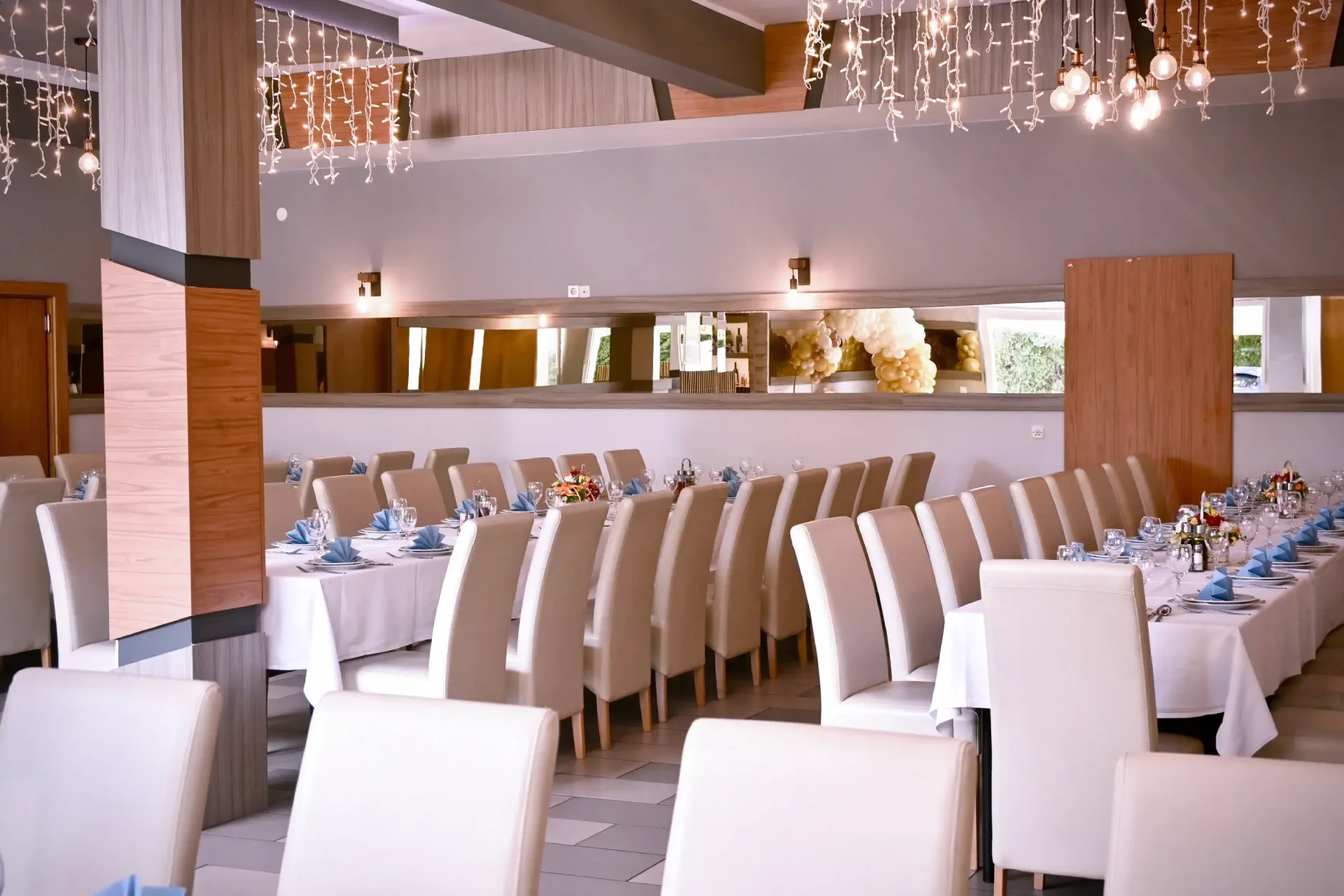 Kod Bosanca velika sala sa redovima posloženih stolaca i stolova priređenih za događanje (bijeli tanjuri, beštek i modre salvete) sa redovima posloženih stolaca i stolova priređenih za događanje (bijeli tanjuri, beštek i modre salvete)