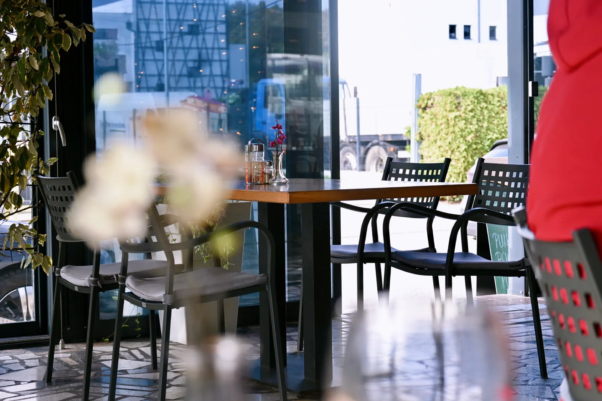 Fotografija crnih stolaca i svijetlosmeđih stolova na terasi sa bočicama za ocat i ulje na stolu