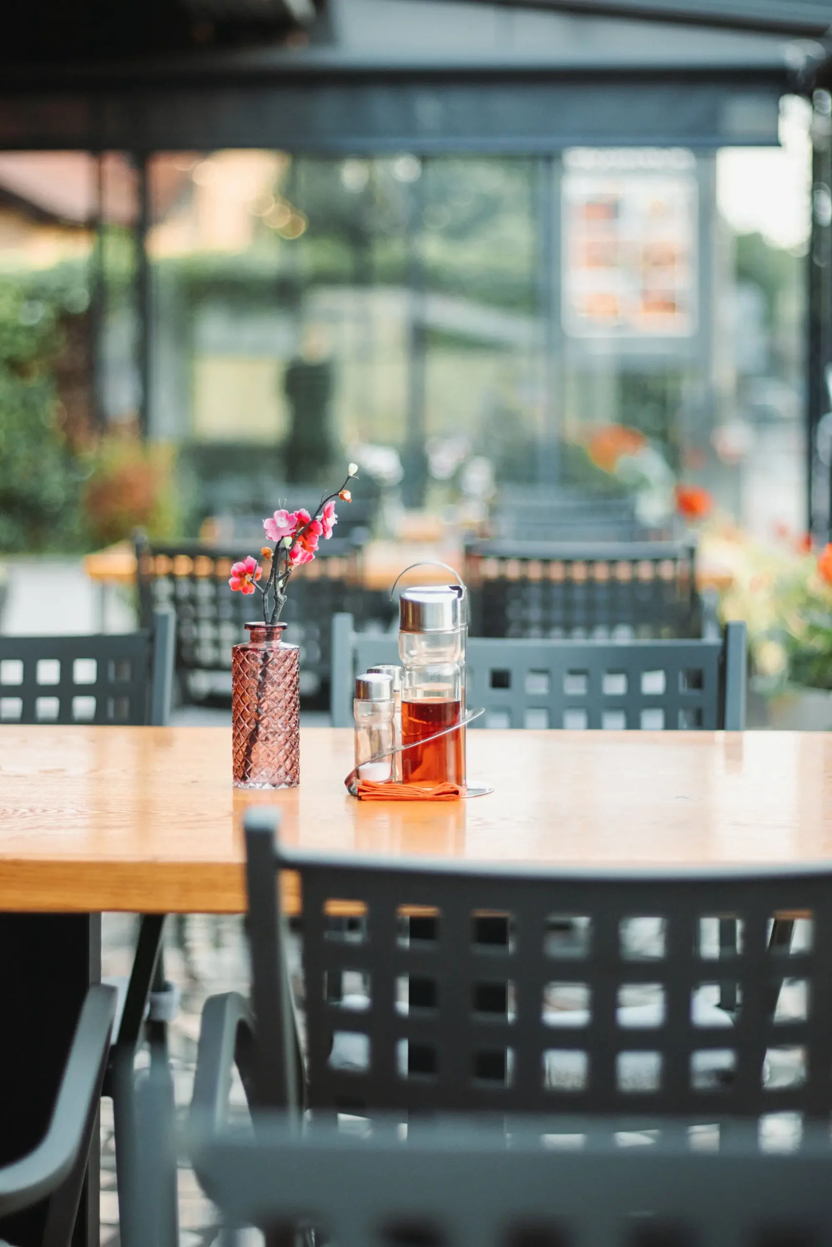 Fotografija crnih stolaca i svijetlosmeđih stolova na terasi sa bočicama za ocat i ulje na stolu