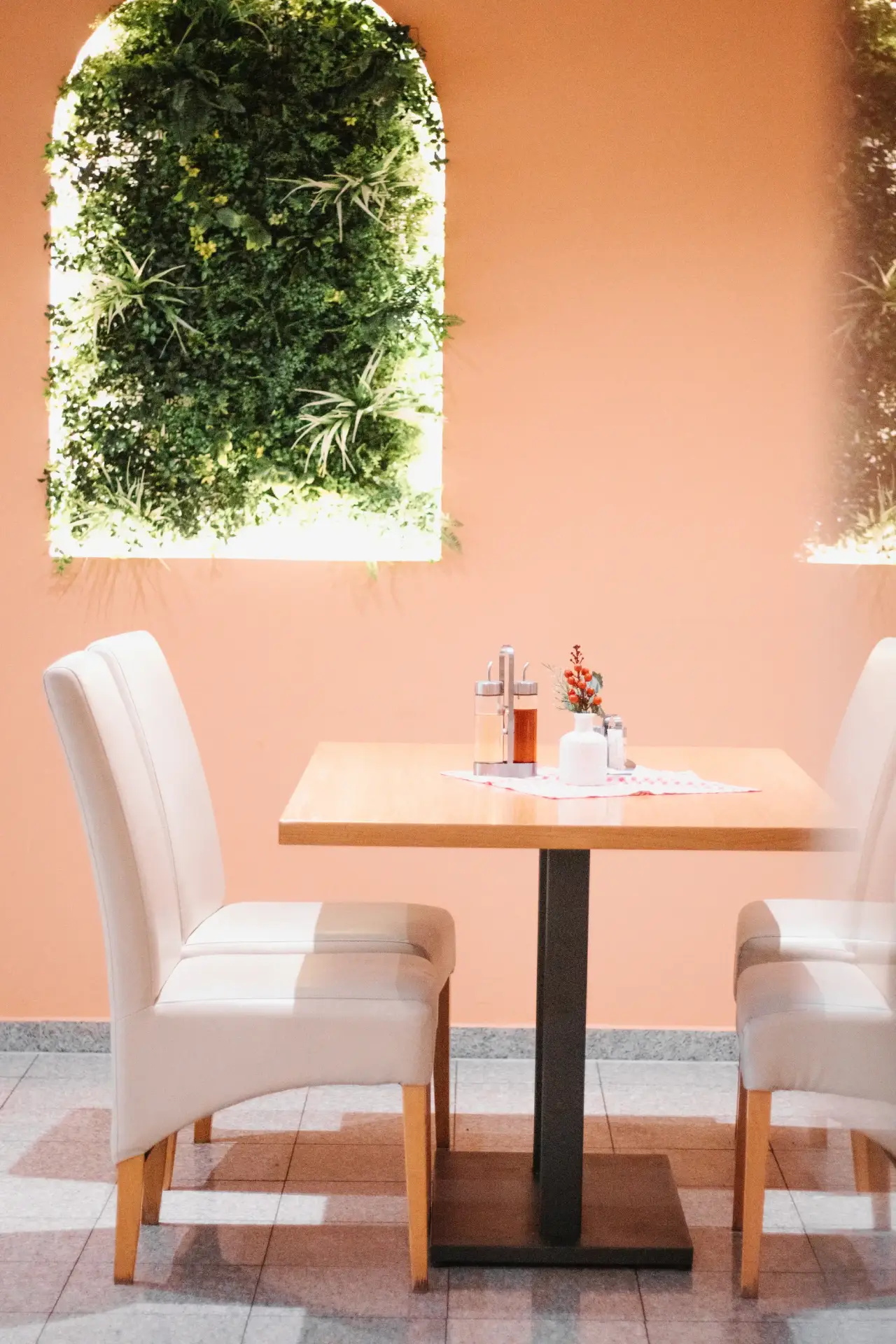 Na slici je prikazana žuto-oker ofarbana prostorija sa svijetim sivkastim stolicama i natur-drvo stolovima a po zidu su zelene florealne strukture