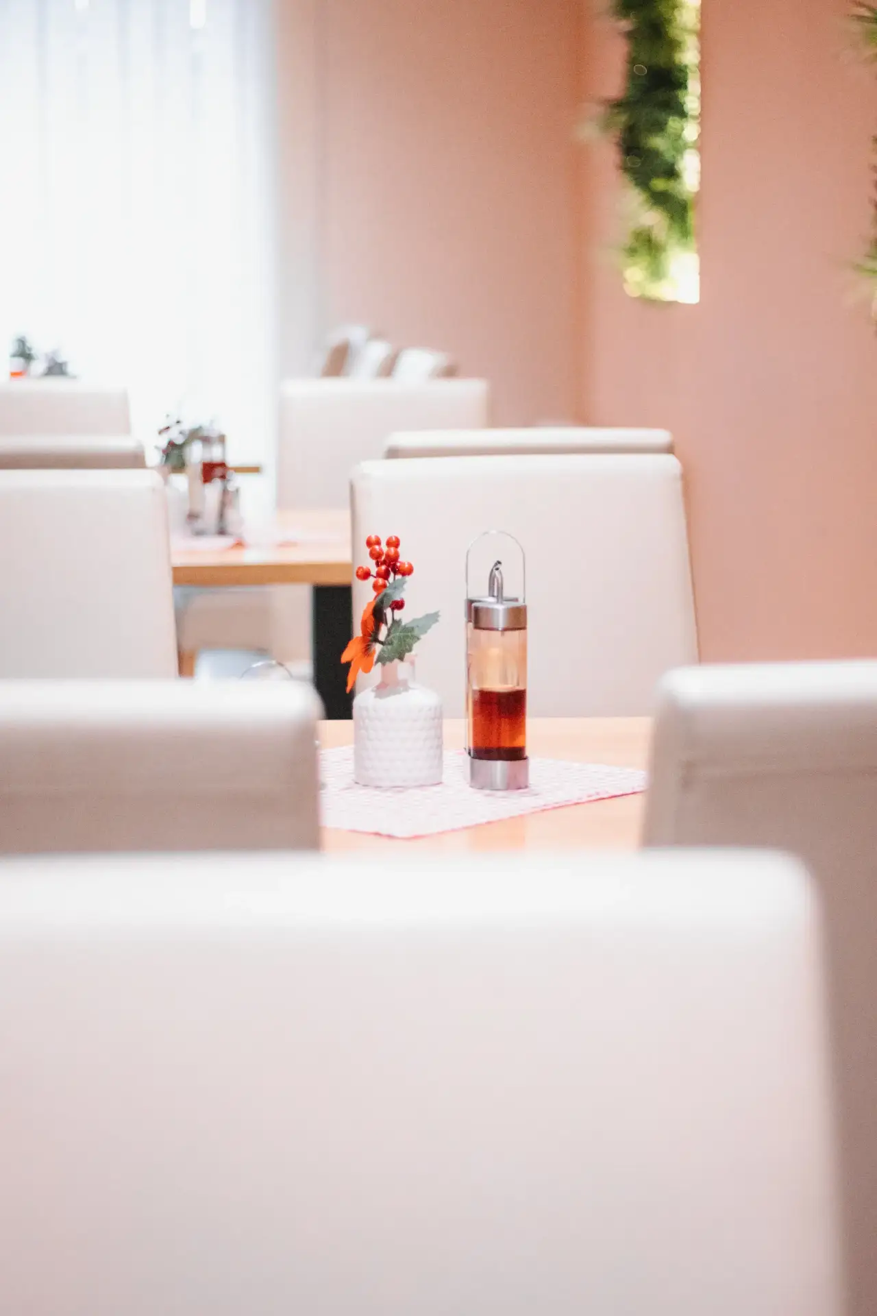 Na slici je prikazana žuto-oker ofarbana prostorija sa svijetim sivkastim stolicama i natur-drvo stolovima na kojima se nalaze bočice sa octom i uljem